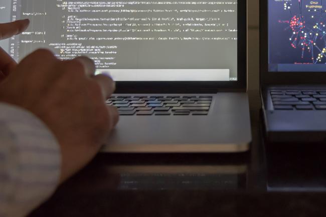 A programmer working at two laptop screens with code displayed on