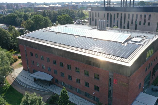 Aerial photo showing the solar panels on the roof of the Earlham Institute building, the sun reflecting off the corner of the building.