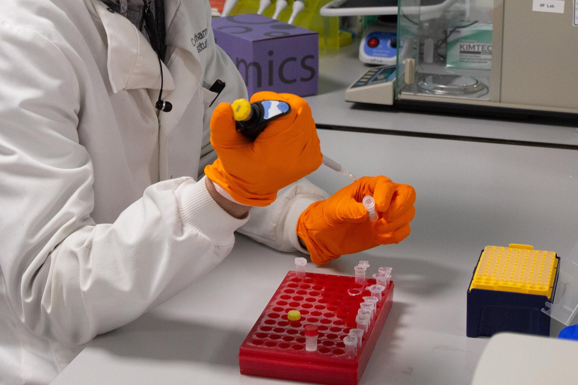 Scientist wearing white lab coat and orange safety gloves working on DNA extraction in the labs